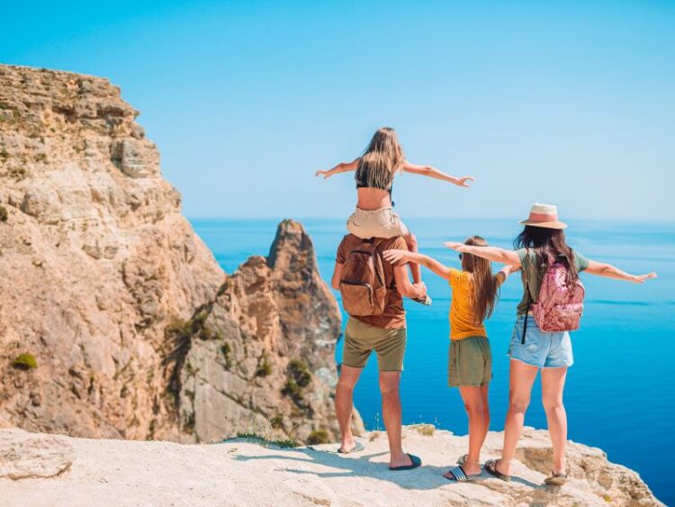 Family standing on a cliff overlooking the ocean, creating unforgettable bonding moments on a stress-free family vacation.
