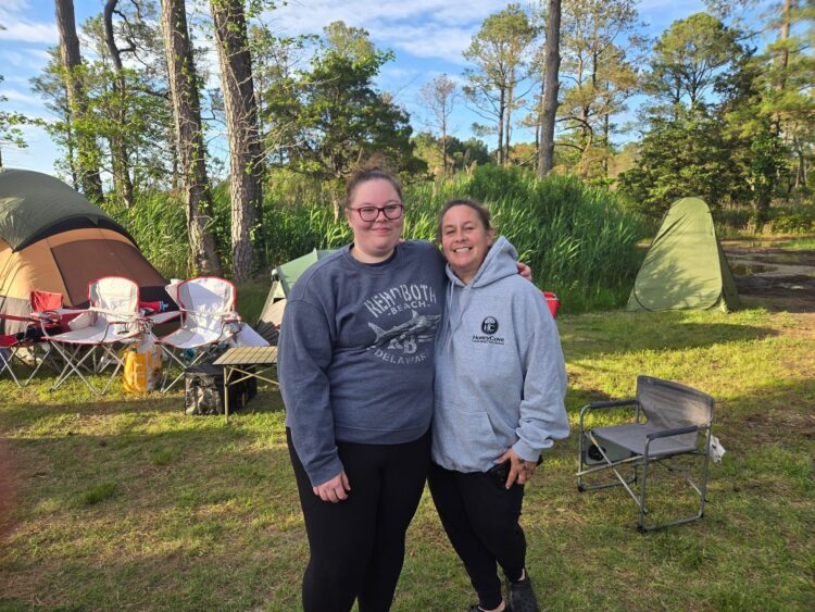 Family campsite at Point Lookout State Park with tents and chairs set up among tall trees and marsh grasses in Maryland.
