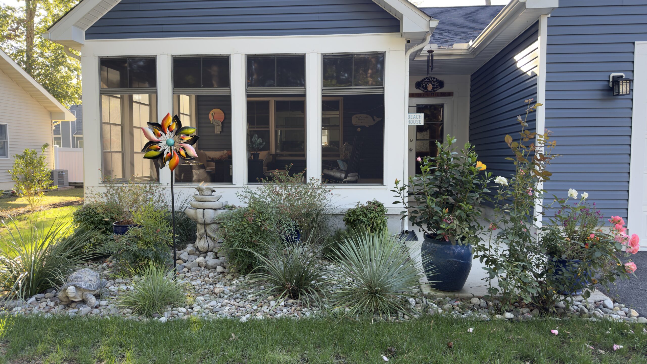 Cozy coastal home exterior at sunset with soft porch lighting, Adirondack chairs, and a welcoming garden pathway, creating a peaceful, lived-in atmosphere ideal for mindful living and home sanctuary inspiration.