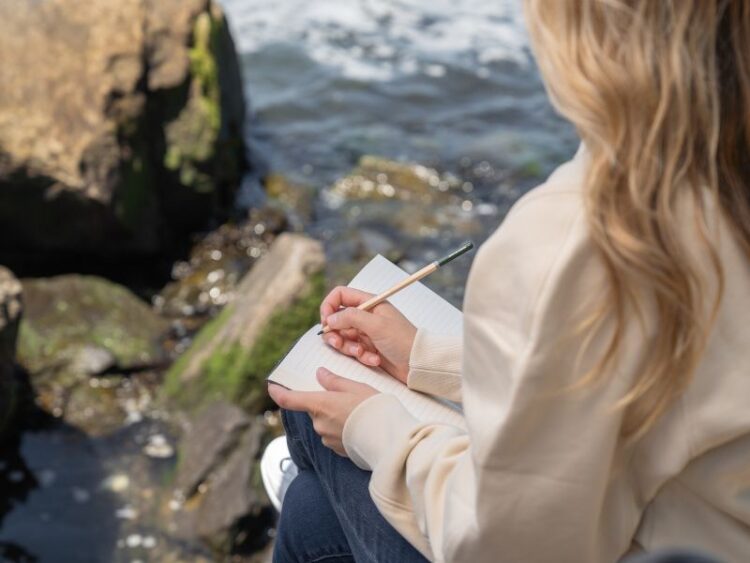 Woman sitting on a bench journaling while traveling slowly, mindful reflection in nature