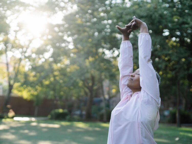 Woman stretching outdoors at sunrise during mindful travel wellness retreat