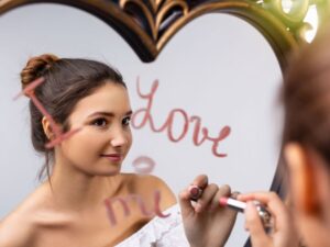 Woman writing "I love you" on a mirror with lipstick as a self-love affirmation