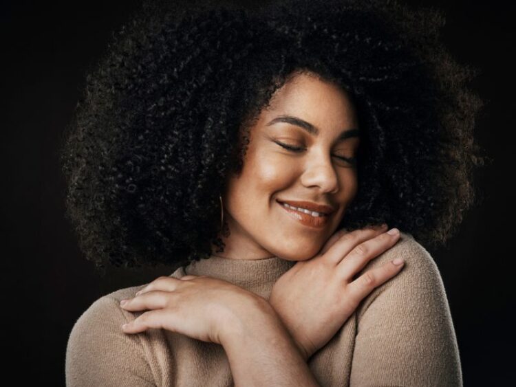 Young woman with curly hair hugging herself and smiling, representing self-love and confidence
