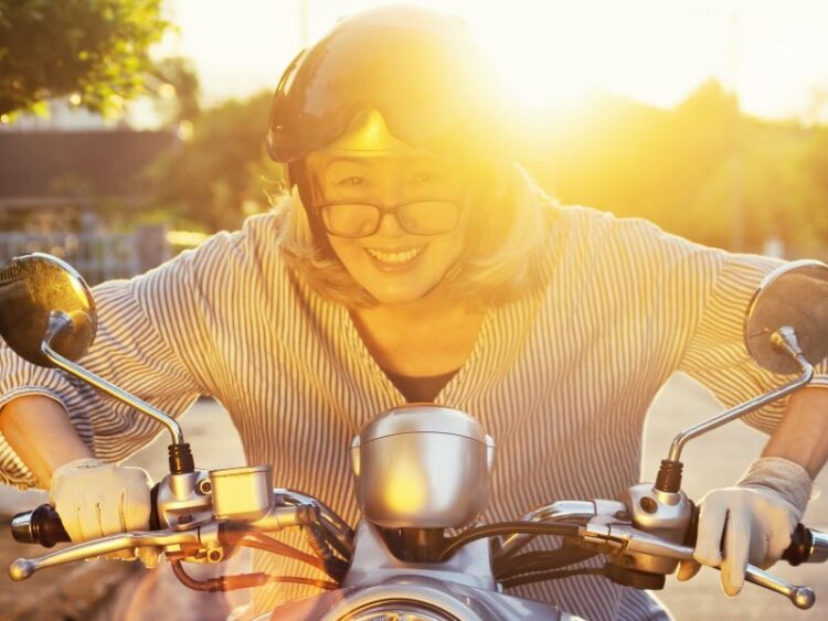 Smiling woman riding a motorbike at sunset, embracing freedom and joy