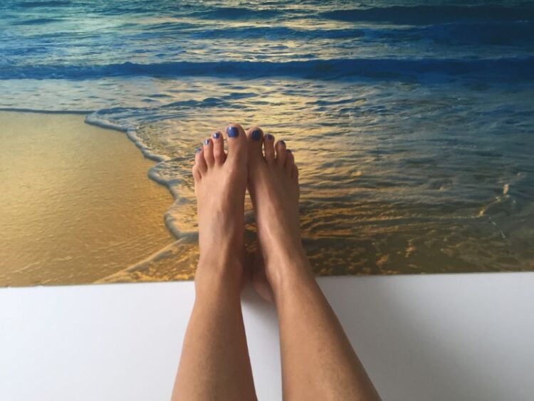 Relaxed feet by the shoreline at sunset, symbolizing the mindset shift of making vacation a priority for balance, rest, and renewal.