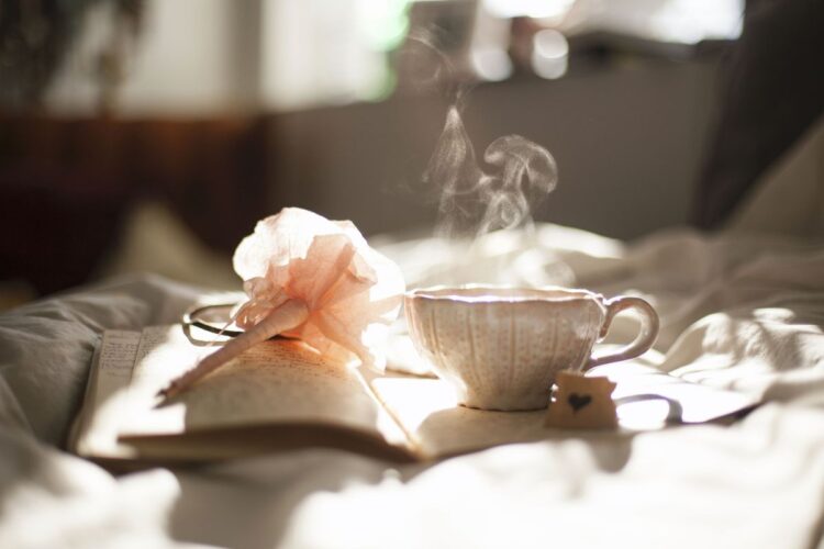 Cozy self-care scene with tea, journal, and morning light on a bed, capturing the essence of personal rituals and reflection