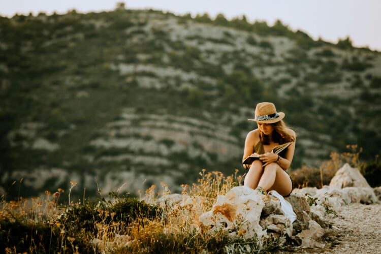 Woman enjoys a peaceful reading moment in a scenic mountain setting, embodying the essence of digital detox travel and summer leisure.
