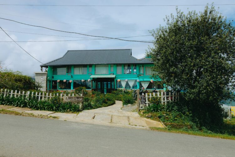 Vibrant green guest house surrounded by lush greenery and a serene road setting with cozy design and local character.