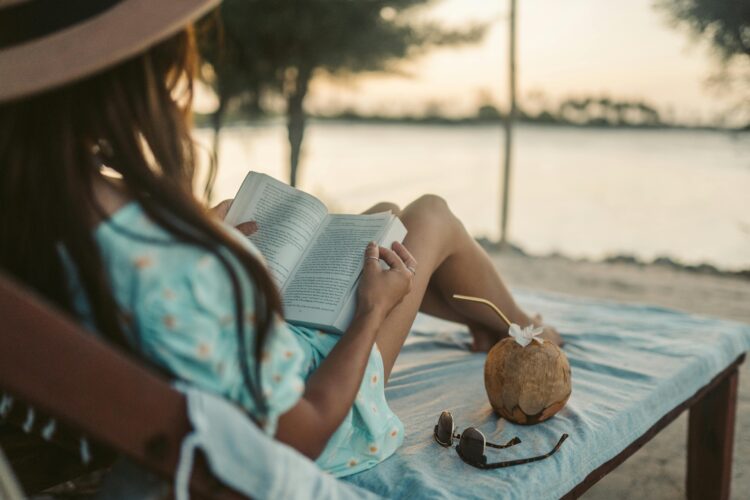 Woman enjoys a peaceful sunset reading session on Zanzibar beach with a coconut drink nearby, capturing the essence of digital detox travel.