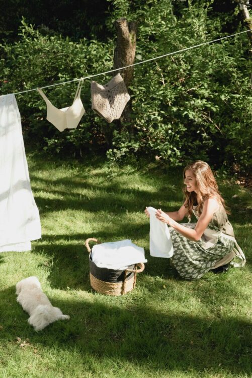 A woman folds laundry in a sunny yard with clothes drying on a line. 
