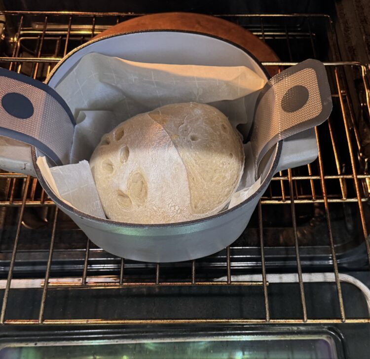 Sourdough bread baking in a Dutch oven on parchment paper and oven silicone sling inside the oven. Parchment paper was not needed.