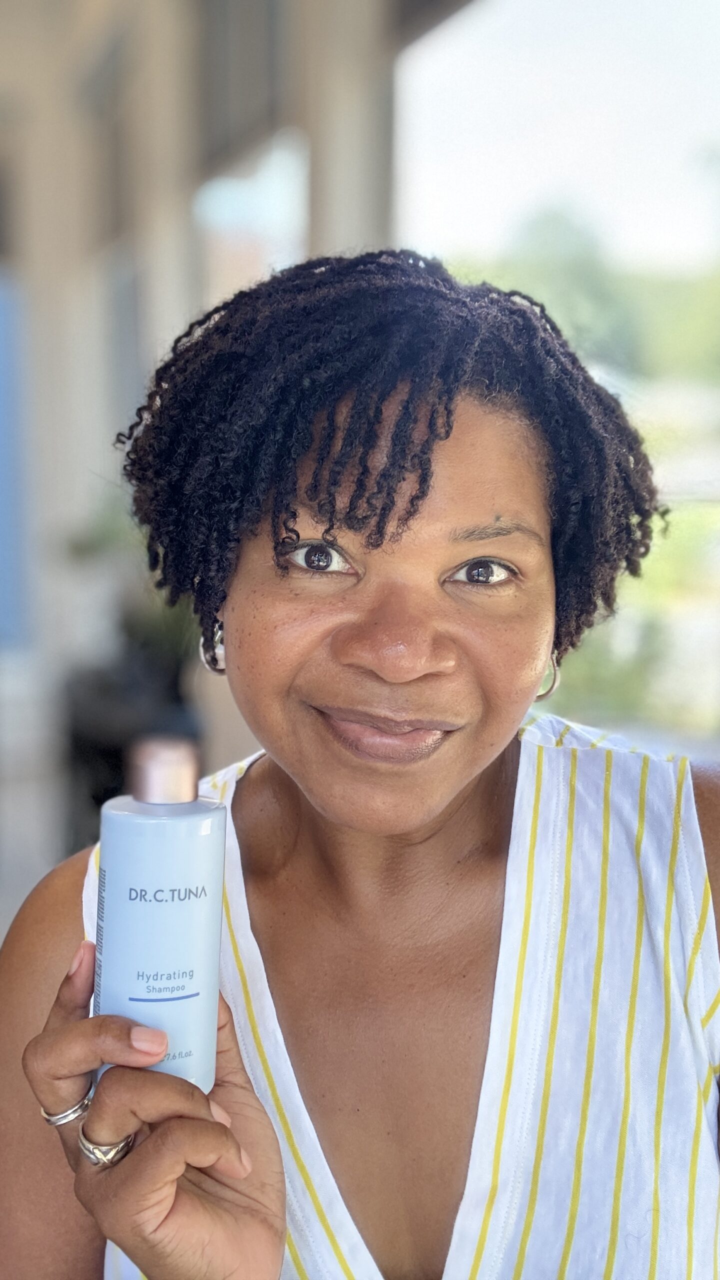 Woman with microlocs holding Farmasi Dr. C. Tuna Hydrating Shampoo, showcasing affordable clean beauty for intentional living and simpler haircare routines.
