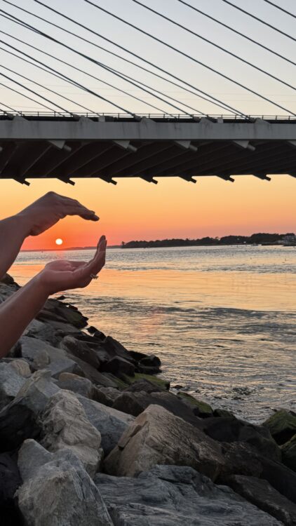 mindful living sunset reflection by the water with hands framing the sun