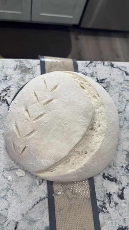 Freshly scored sourdough loaf on a floured surface before baking, showing open crumb and artisan design.