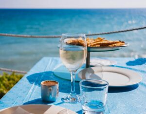 Elegant seaside dining scene with wine, coffee, and pastries on a sunny day.
