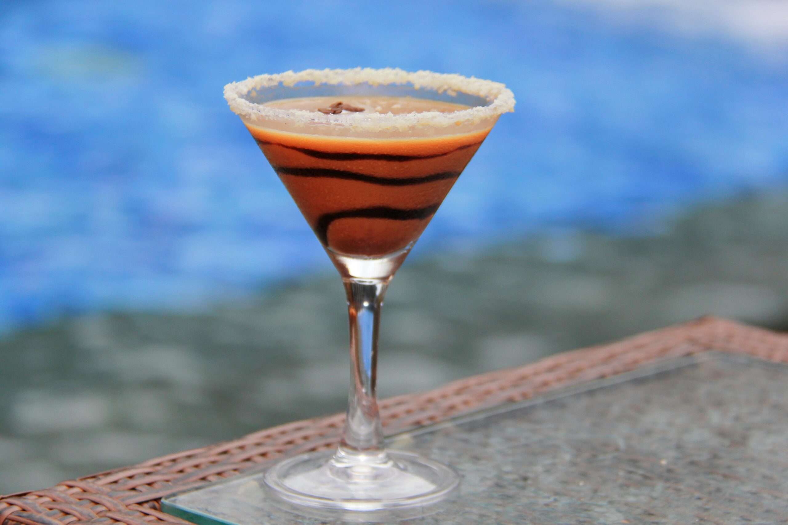 A decadent chocolate martini with a sugar rim beside a serene pool.