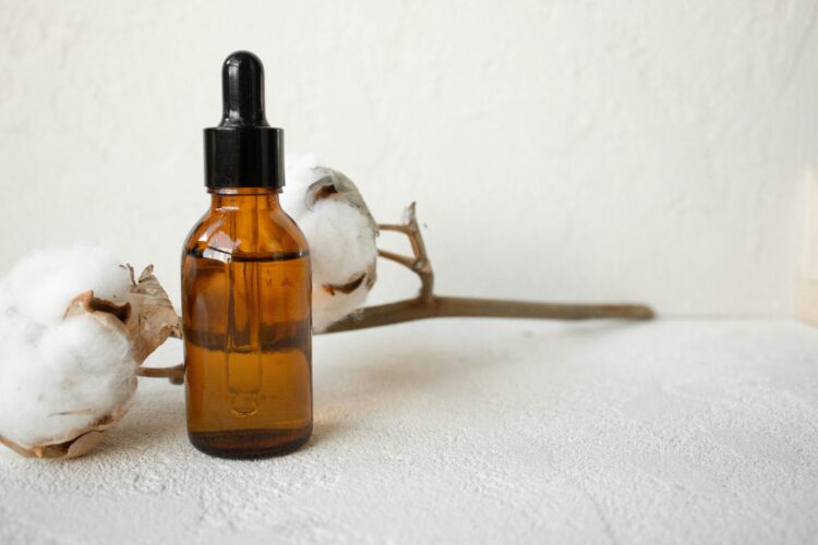 Brown glass dropper bottle with cotton branch on white textured surface.