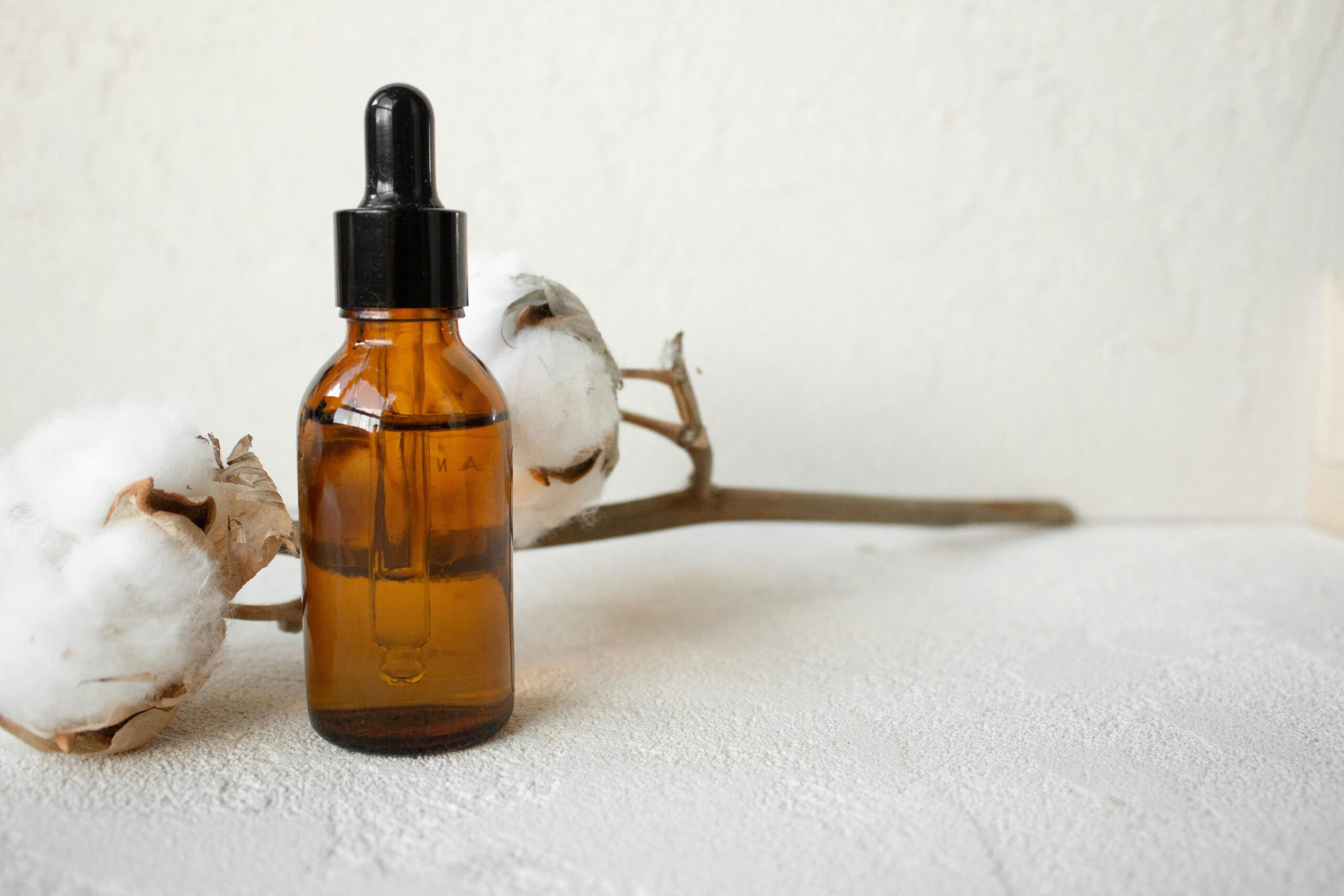 Brown glass dropper bottle with cotton branch on white textured surface.