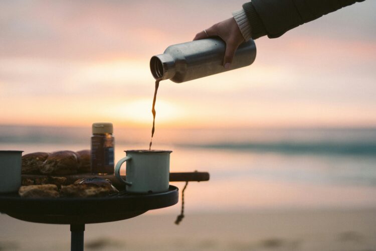 Enjoying a hot coffee in a rustic mug on the beach at sunrise, capturing a peaceful morning moment.