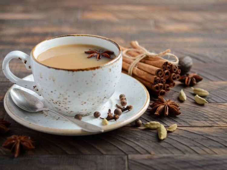 A ceramic cup of creamy chai tea on a rustic wooden table surrounded by cinnamon sticks, cardamom pods, and star anise.