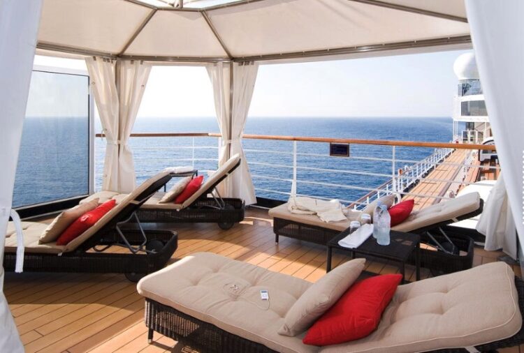 Private cabana deck aboard a cruise ship overlooking calm blue ocean waters, with soft sunlight, lounge chairs, and a peaceful open-sea view — an inviting space for rest and restoration