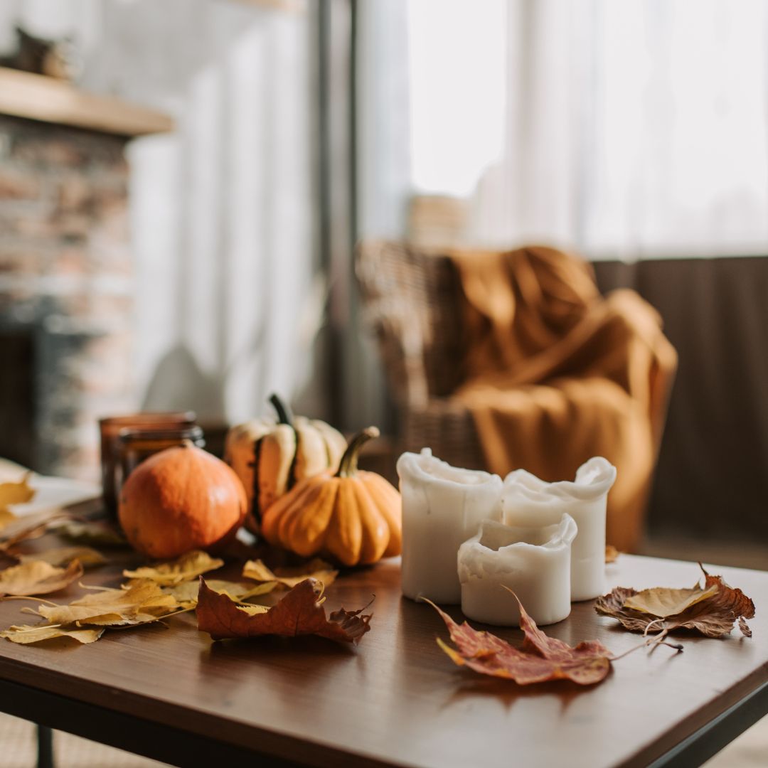 A cozy living room with candles, pumpkins, and fall leaves on a wooden table, capturing a peaceful atmosphere perfect for a holiday mindful evening routine.