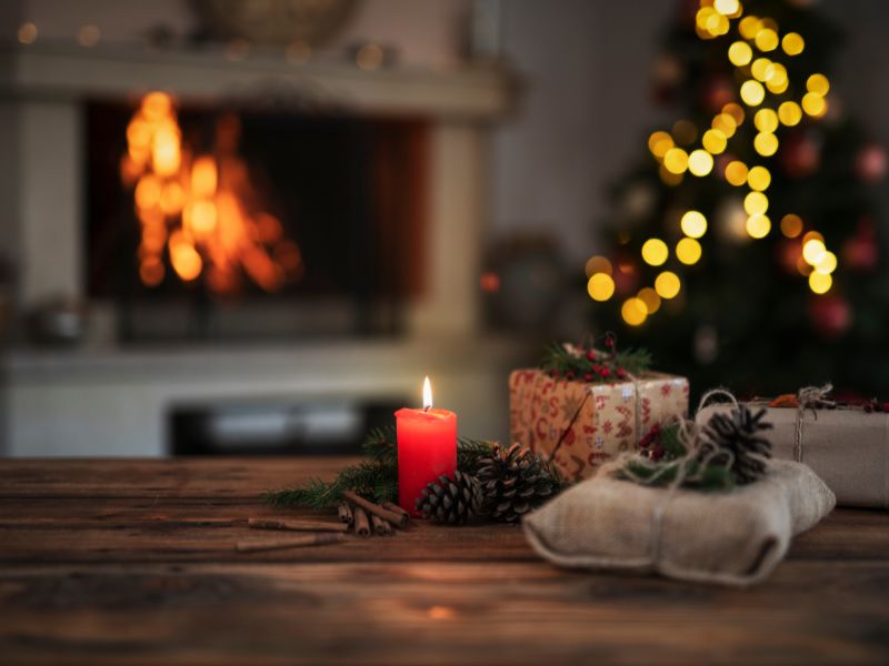 Cozy holiday scene with a lit candle, rustic wrapped gifts, pinecones, and a softly glowing Christmas tree near a fireplace, representing mindful living for the holidays.