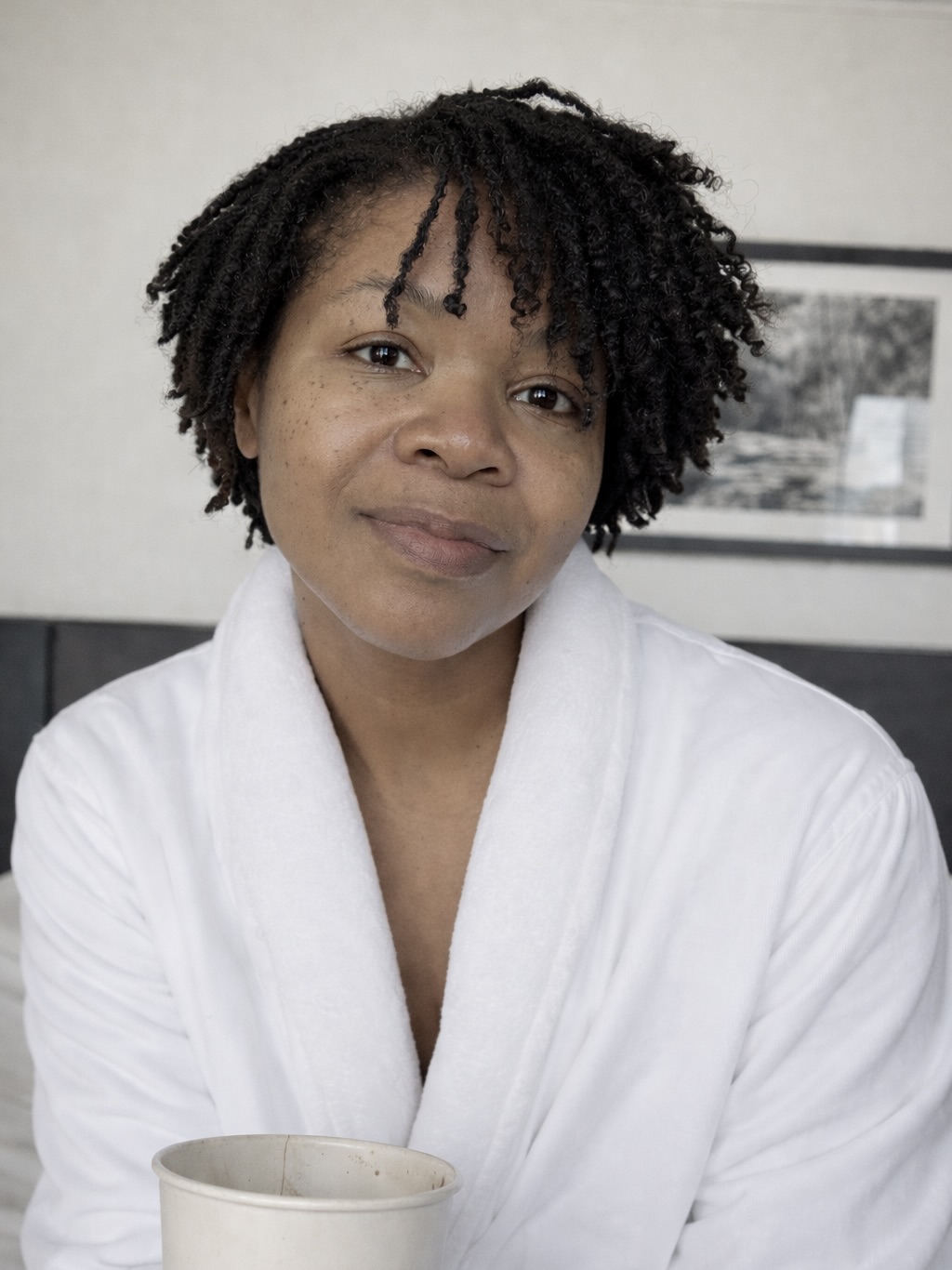 Subrinia Pierpont, founder of Live Thrive Travel, resting in a white robe with a warm drink in soft natural light