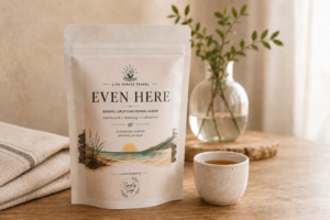 Even Here herbal tea by Live Thrive Travel displayed with a warm cup of tea, soft linen, and natural greenery in a calming, neutral setting.