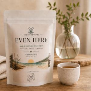 Even Here herbal tea by Live Thrive Travel displayed with a warm cup of tea, soft linen, and natural greenery in a calming, neutral setting.