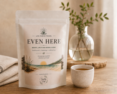 Even Here herbal tea by Live Thrive Travel displayed with a warm cup of tea, soft linen, and natural greenery in a calming, neutral setting.