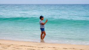 A woman standing in the ocean at the beach while quietly filming the waves during a reflective moment of calm.