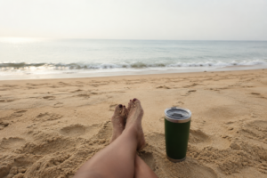 Coffee beside bare feet on a quiet beach, representing a simple morning self-care ritual and the idea that fifteen intentional minutes can make a difference.